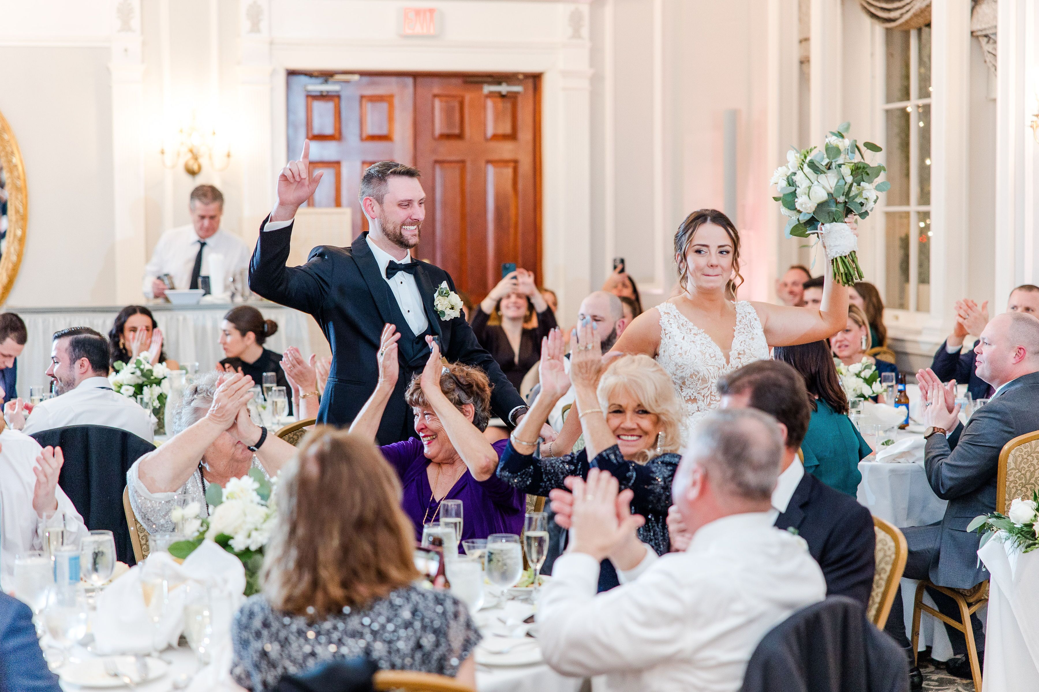 A formal event with guests seated at round tables, clapping, and a couple in the foreground.