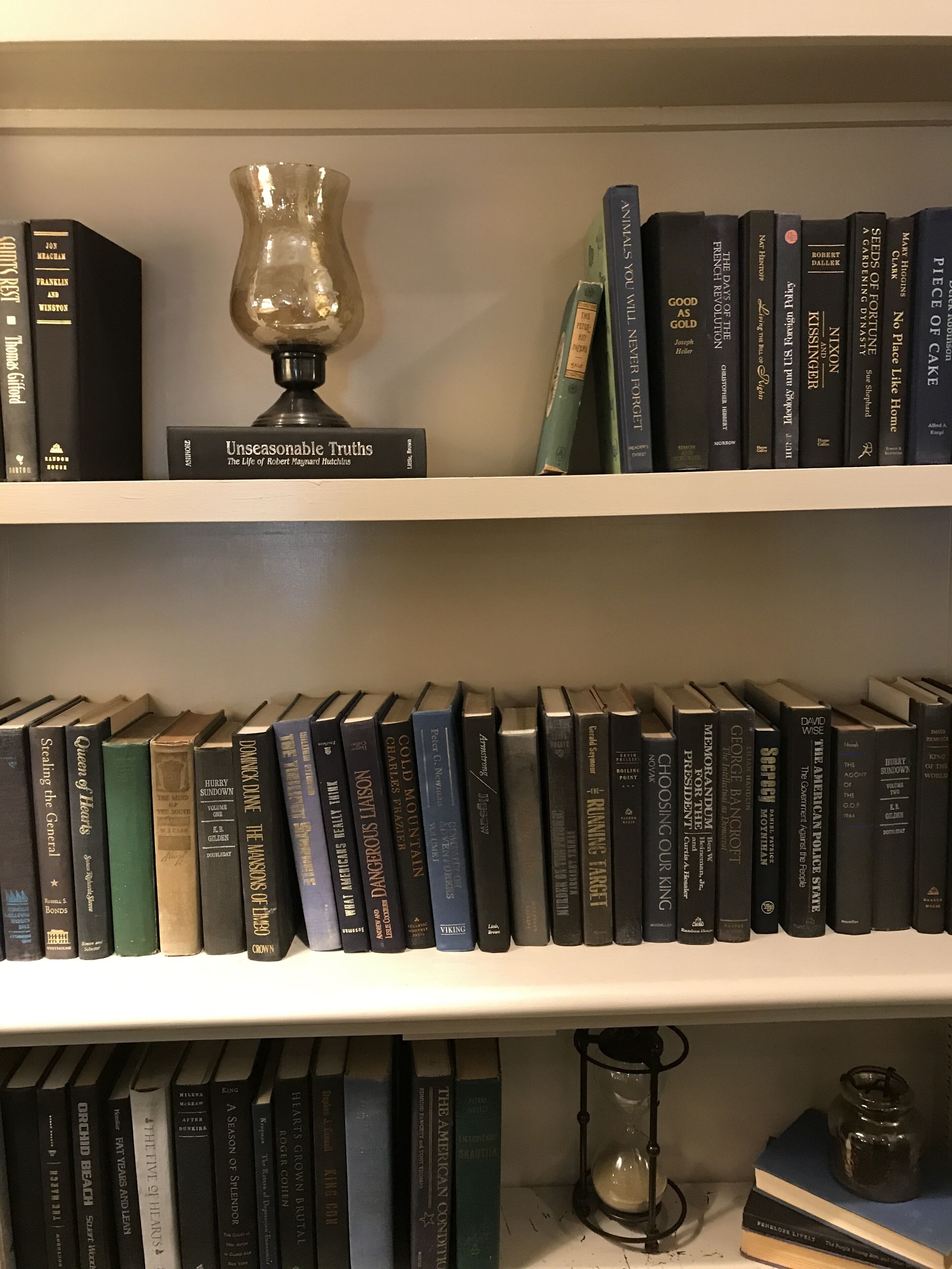 A bookshelf with various books, a decorative vase, and a small hourglass.