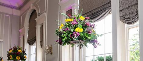 Un salón de banquetes con sillas doradas, manteles morados y centros de mesa florales.