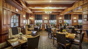 A traditional dining area with wooden paneling, chandeliers, and a patterned carpet.