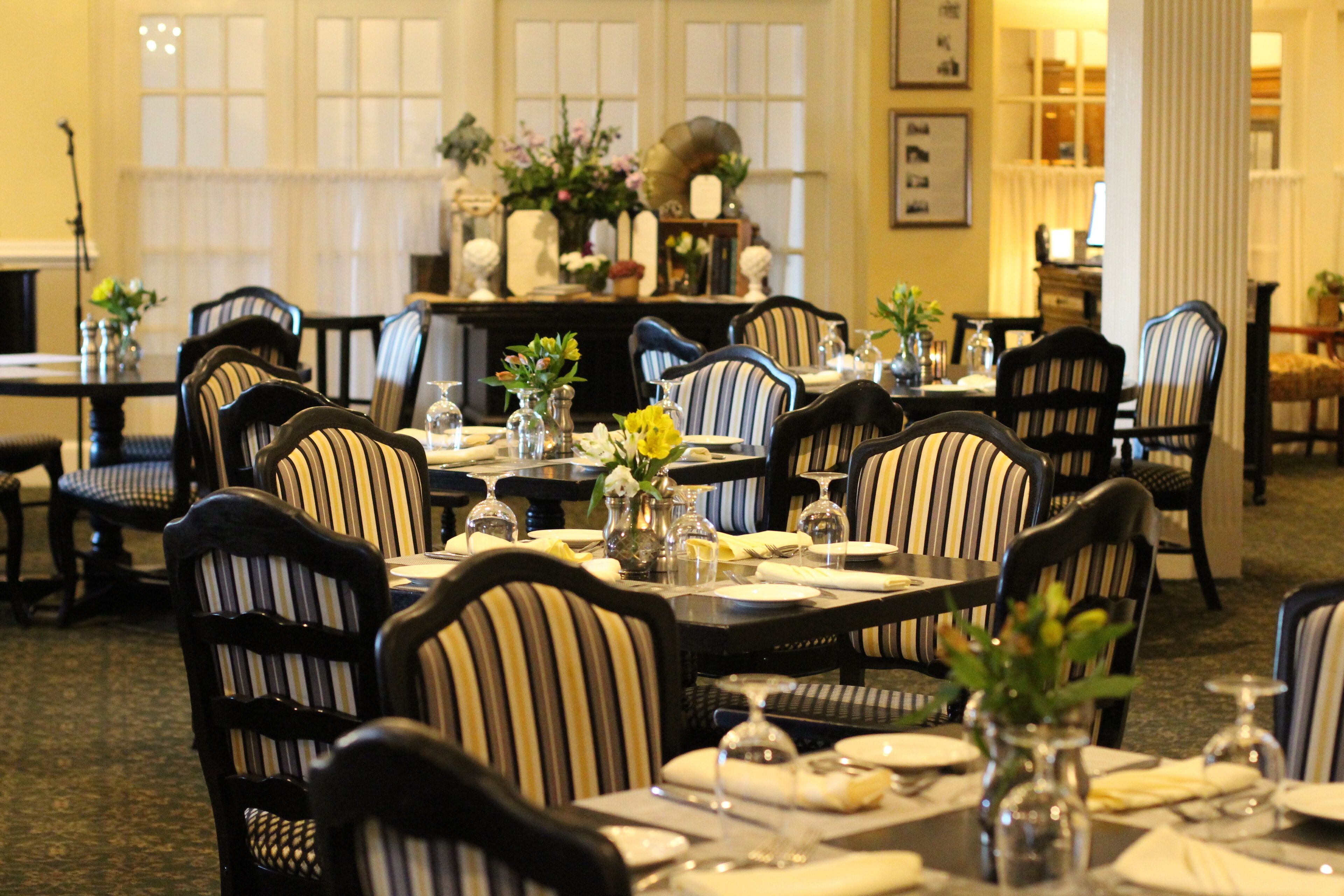 A dining area with striped upholstered chairs, tables set with plates, glasses, and vases of flowers.