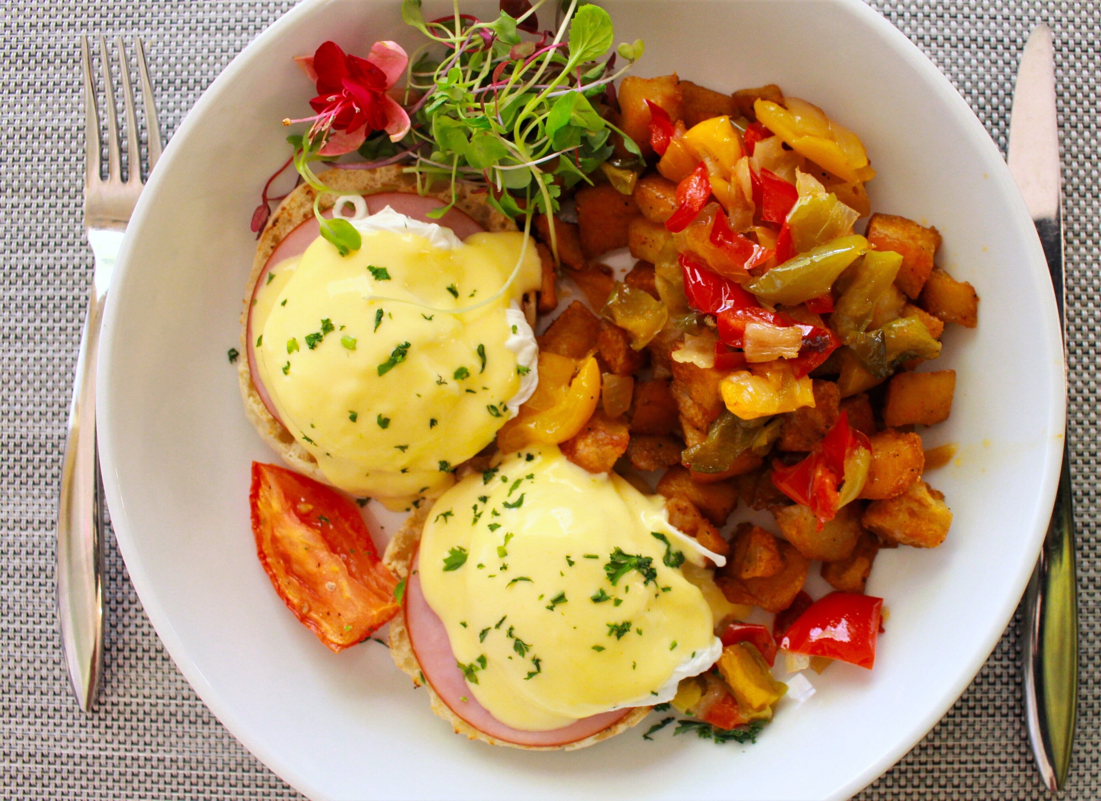A white plate with eggs benedict, hash browns, and mixed vegetables.