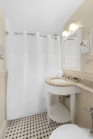 A bathroom with a white sink, a mirror, a towel rack, and a shower curtain. - Hawthorne Hotel (Salem)
