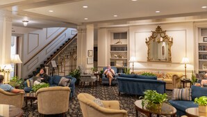 A spacious lobby with multiple seating areas, a staircase, and a large mirror. - Hawthorne Hotel (Salem)