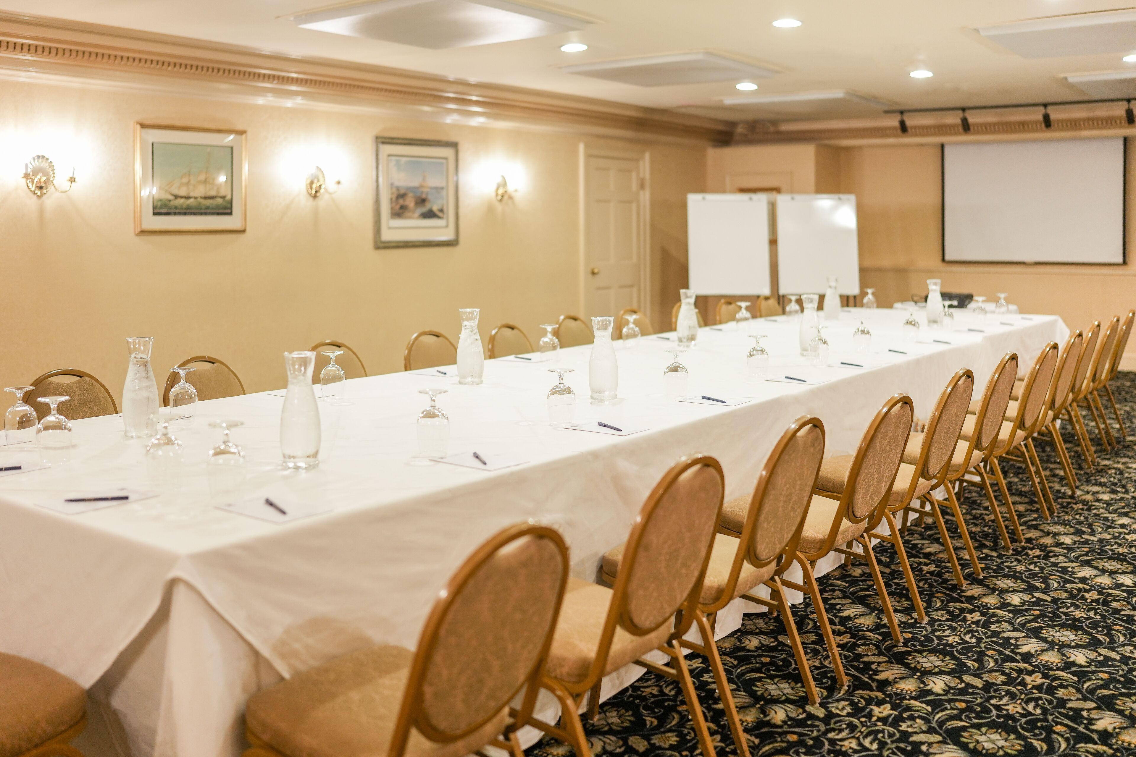 Una sala de conferencias con una mesa larga, sillas y una pantalla para proyector.