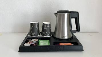 Una bandeja negra con un hervidor de acero inoxidable y dos tazas negras con diseños blancos.