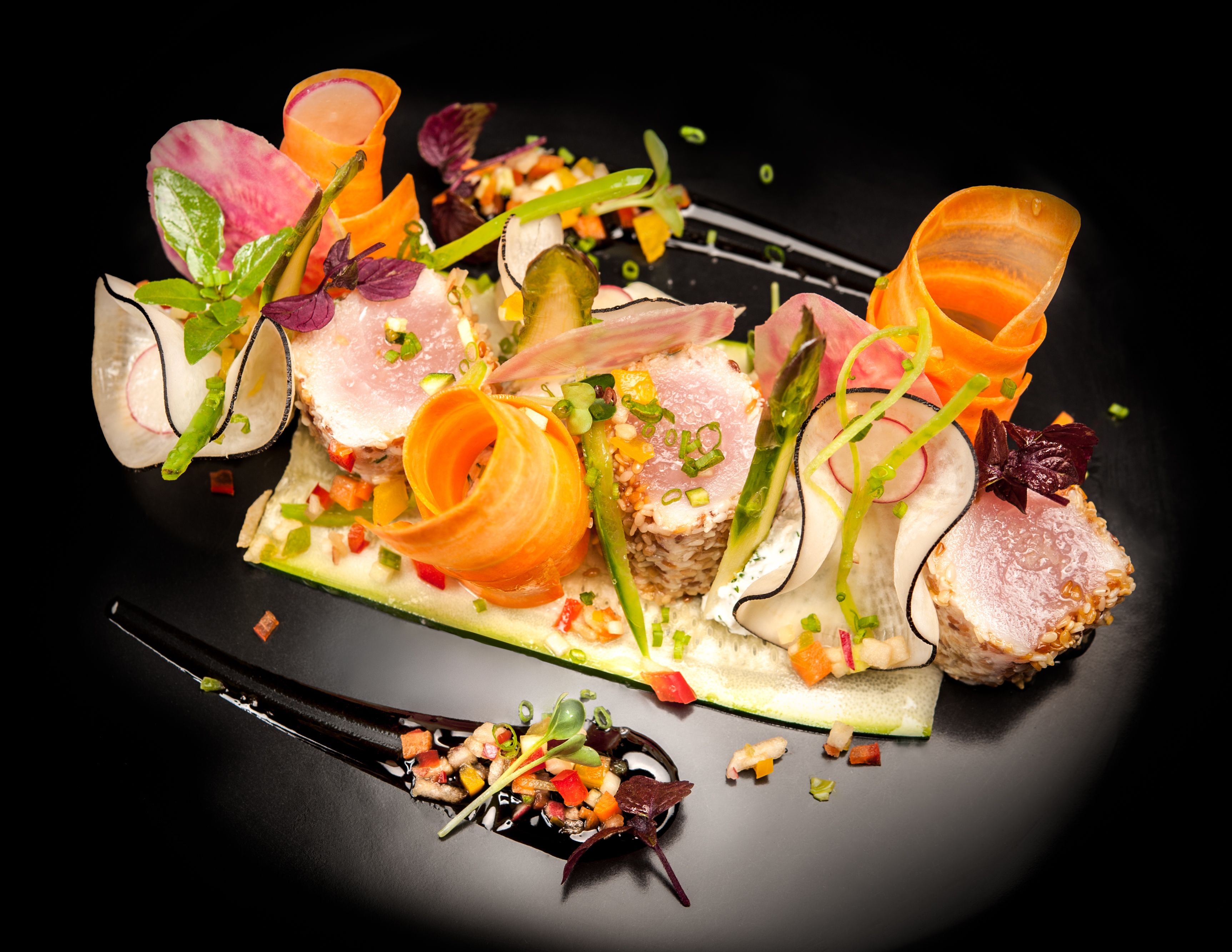 A variety of food items artistically arranged on a black plate.