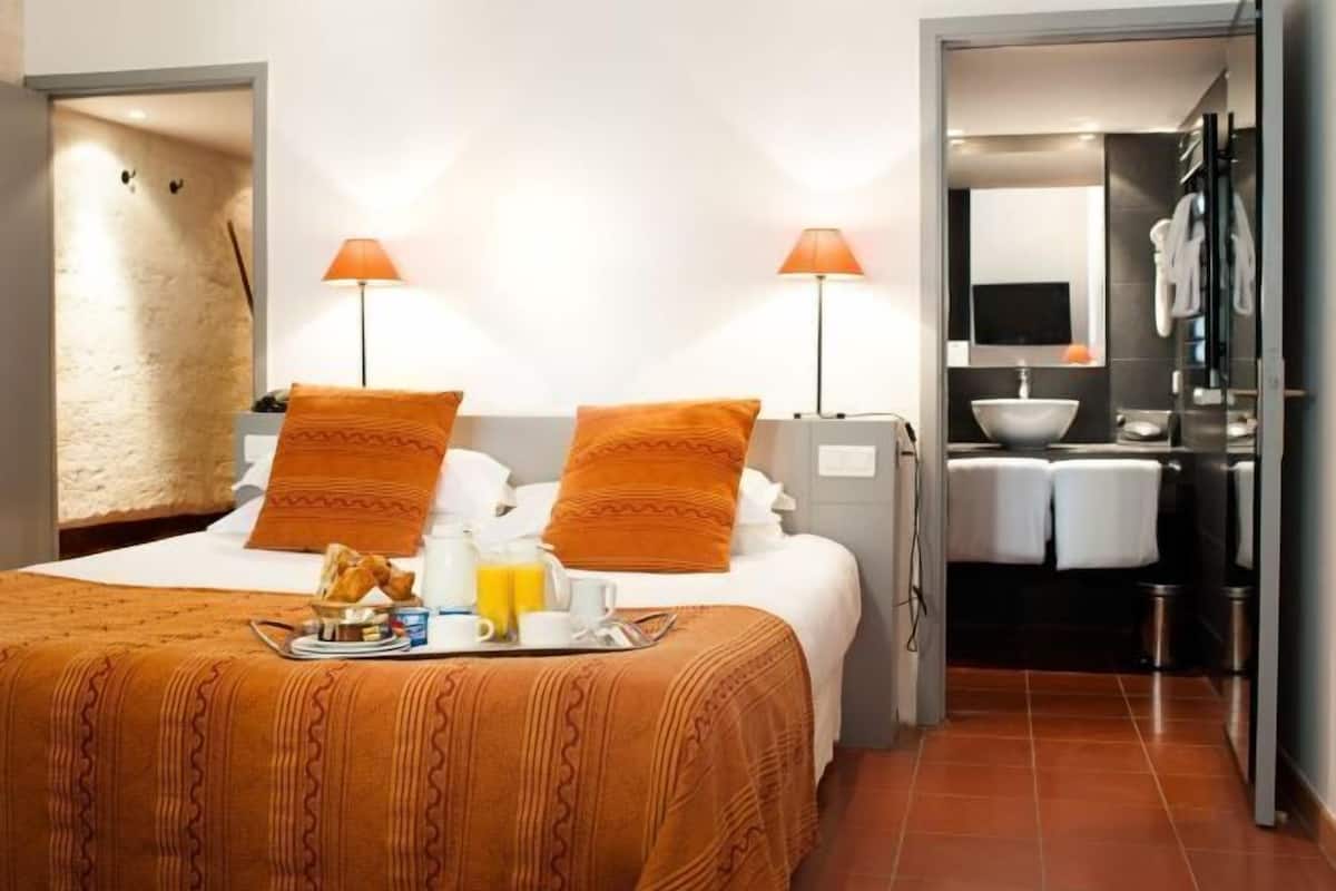 Una habitación de hotel con cama, dos lámparas de noche, una bandeja para el desayuno, un lavamanos y un espejo.
