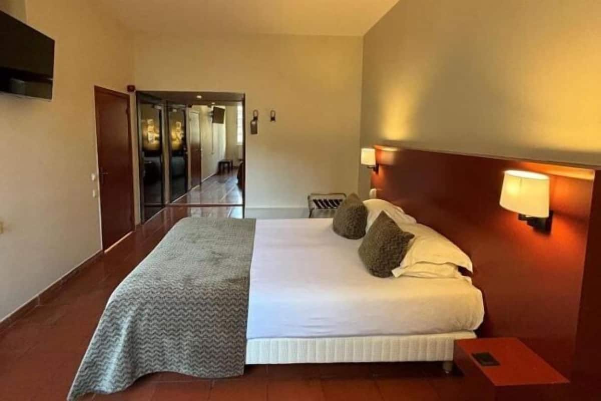 Una habitación de hotel con una cama grande, una mesita de noche, una lámpara y un espejo.