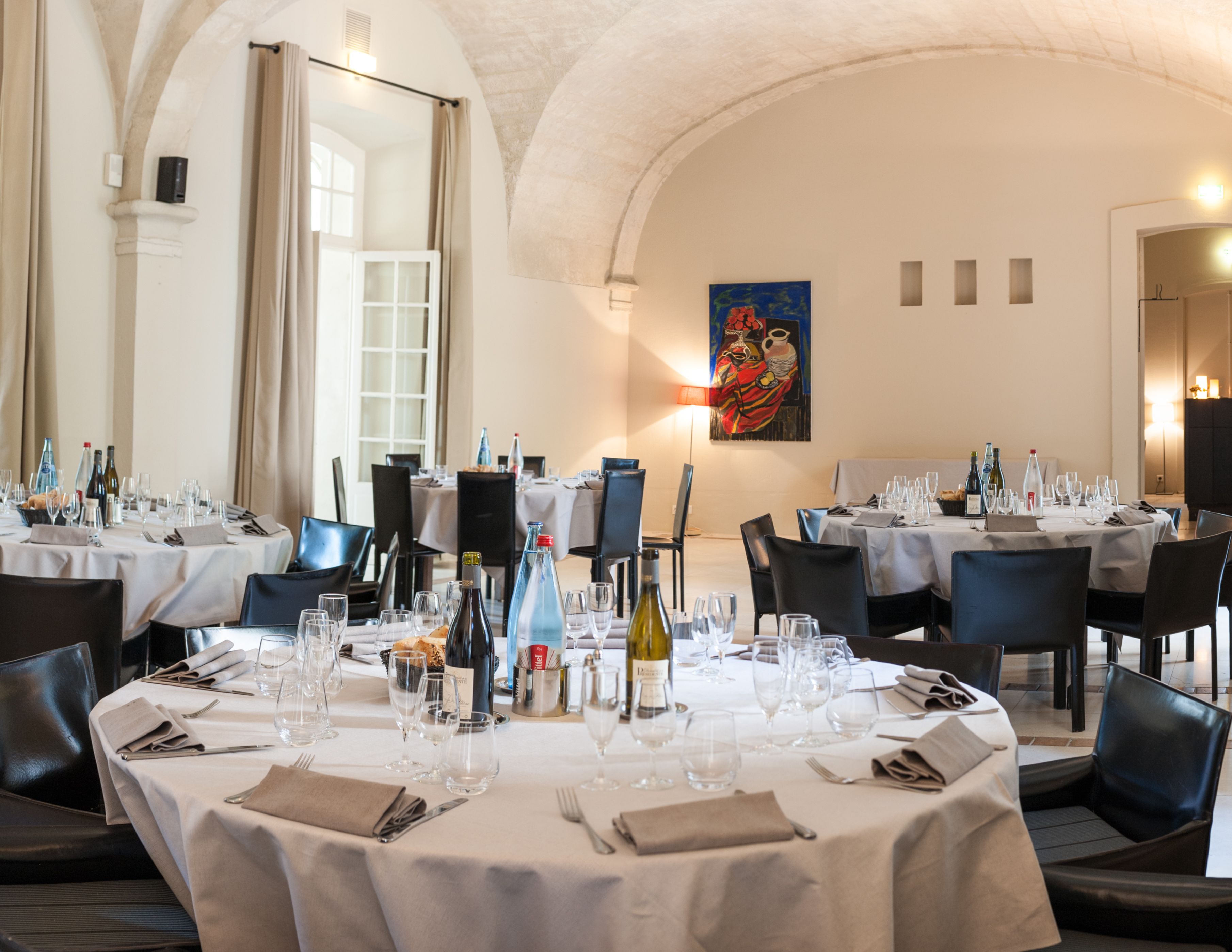 A restaurant with multiple round tables set for dining, featuring white tablecloths and black chairs.