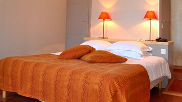 Ein Bett mit einem gemusterten, orangefarbenen Überwurf, zwei Kissen und zwei rote Lampen auf einem Nachttisch.
