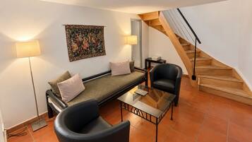Een moderne woonkamer met een bank, een glazen salontafel, een zwarte fauteuil, een trap en een wandtapijt.