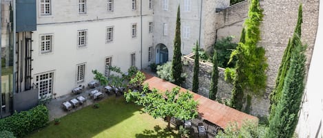 A courtyard with a lawn, outdoor seating, and a building with multiple windows and a stone wall.