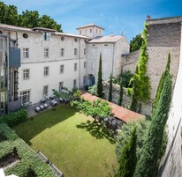 Un patio con césped, mobiliario exterior y un edificio con varias ventanas y una pared de piedra.