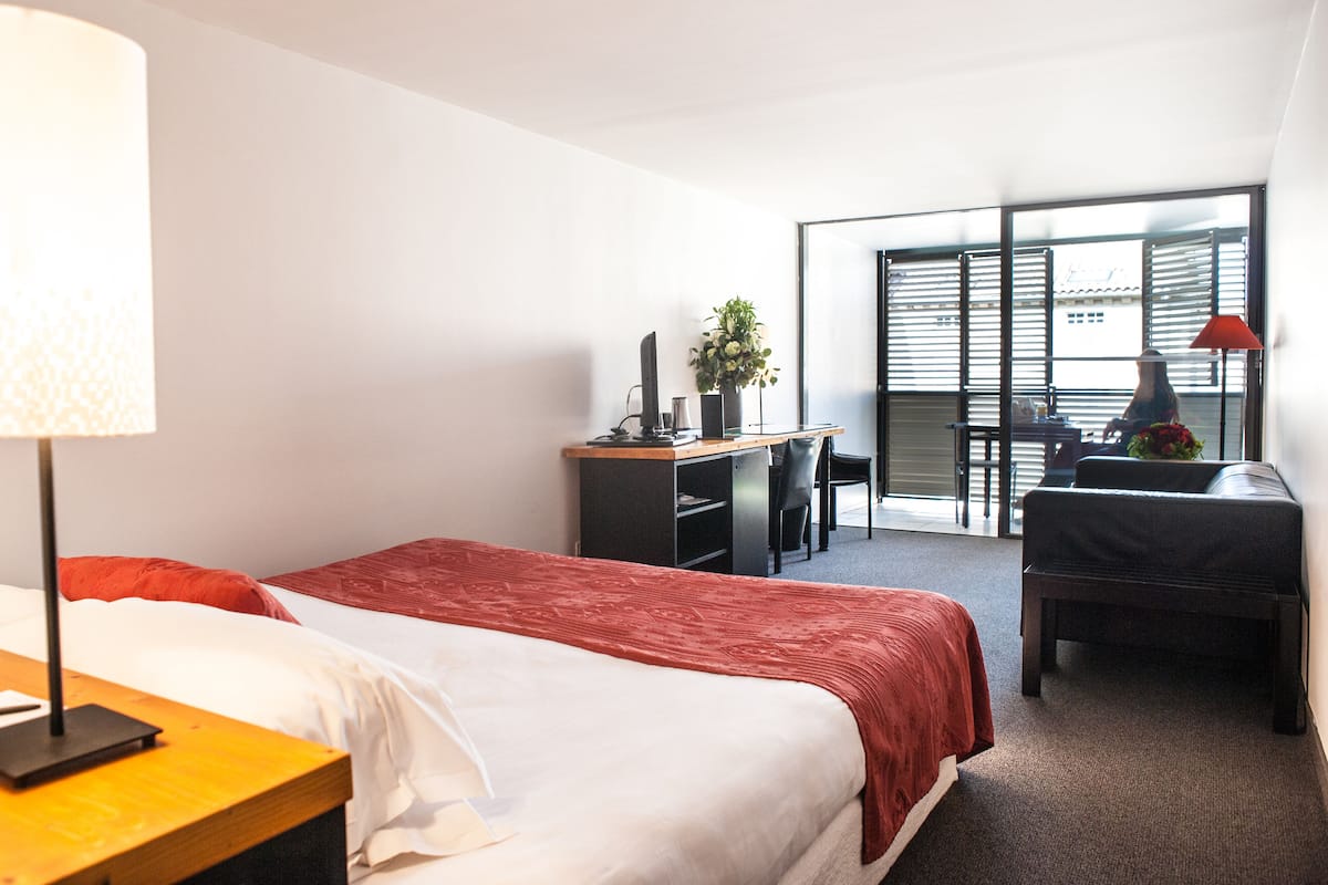 Habitación de hotel con dos camas, un escritorio, una silla, una lámpara y vistas a través de un ventanal grande.