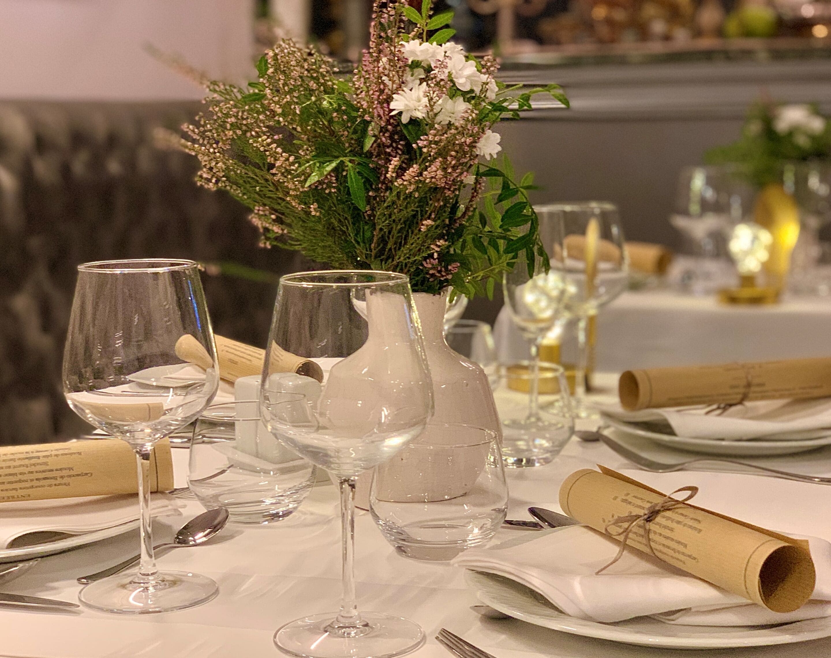 A table set for a meal with wine glasses, a pitcher, and a decorative floral arrangement.