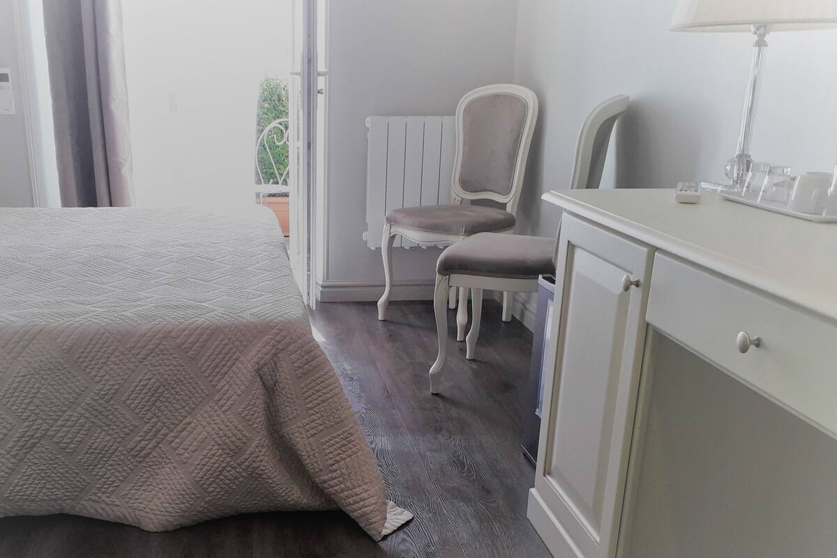 Un dormitorio con cama, una silla, un aparador y una ventana.