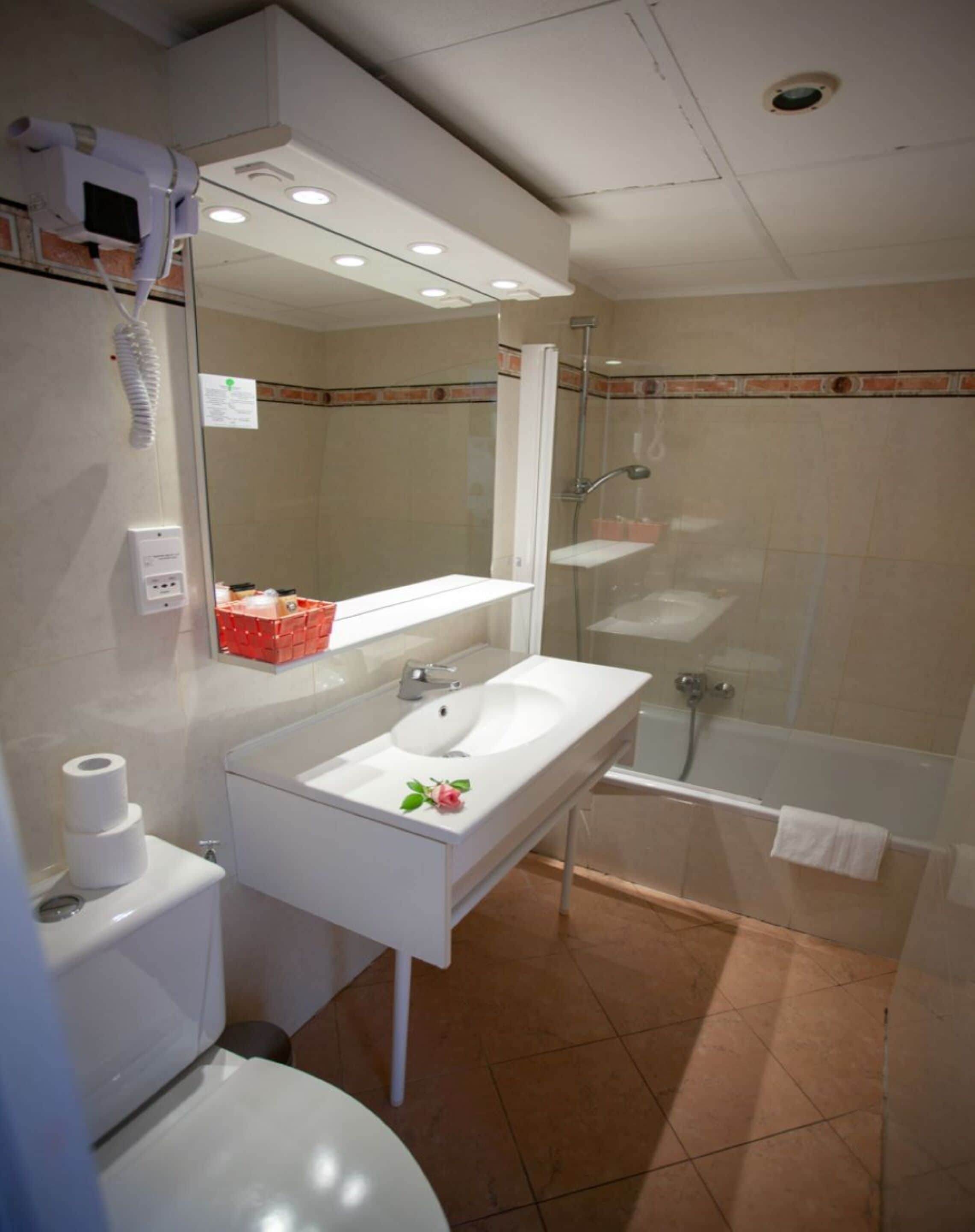 A modern bathroom with a white sink, mirror, and toilet. It includes a shower area with a glass door and a bathtub.