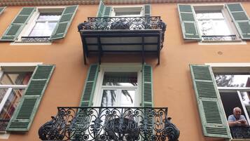Un edificio con balcón, adornado con barandillas de metal negro ornamentadas y contraventanas verdes.