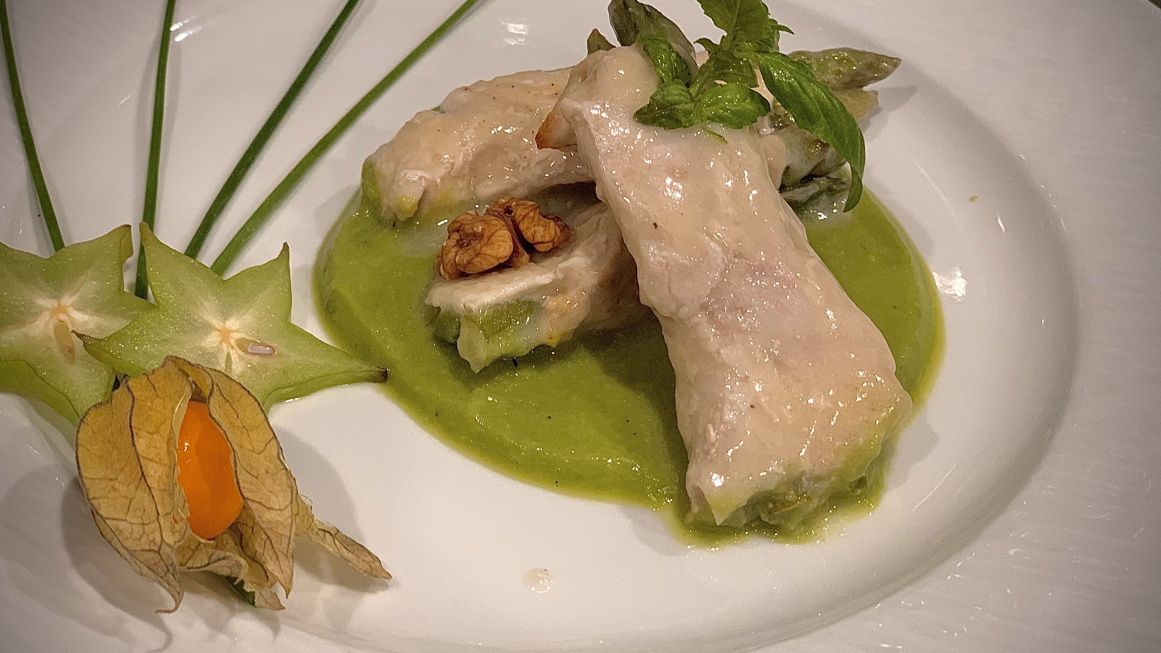 A plate with a dish that includes a green sauce, a piece of meat, and some vegetables.