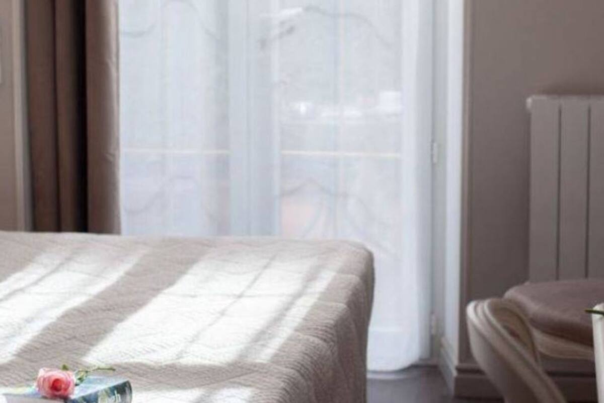 Un dormitorio con una cama, una mesita de noche con un florero, una silla y un radiador.