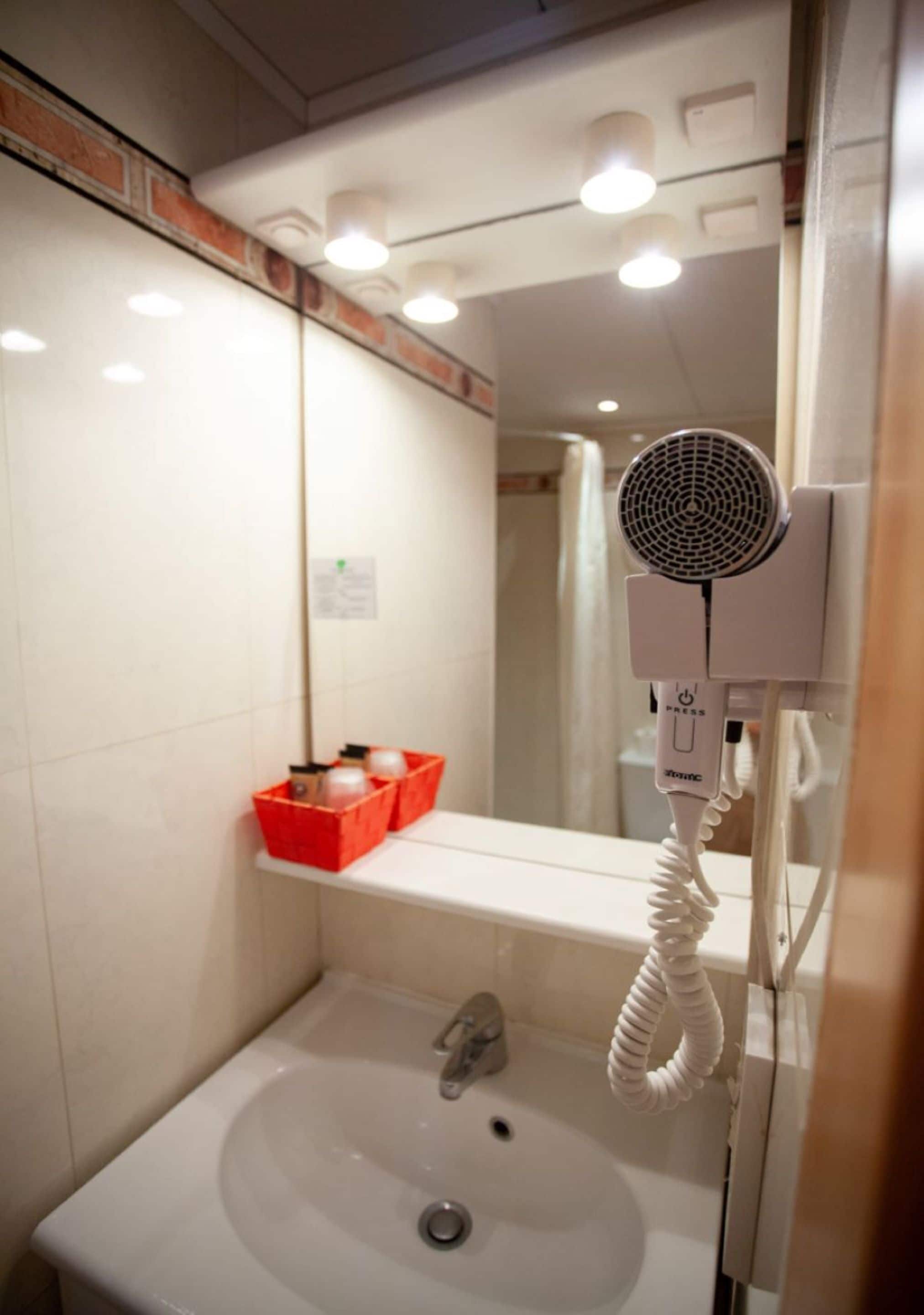 Un baño con un lavamanos blanco, un espejo y un secador de pelo montado en la pared.