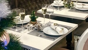 A dining table set with white plates, silverware, and wine glasses, decorated with a small potted plant and pine branches. - Hotel Oasis (Nice)