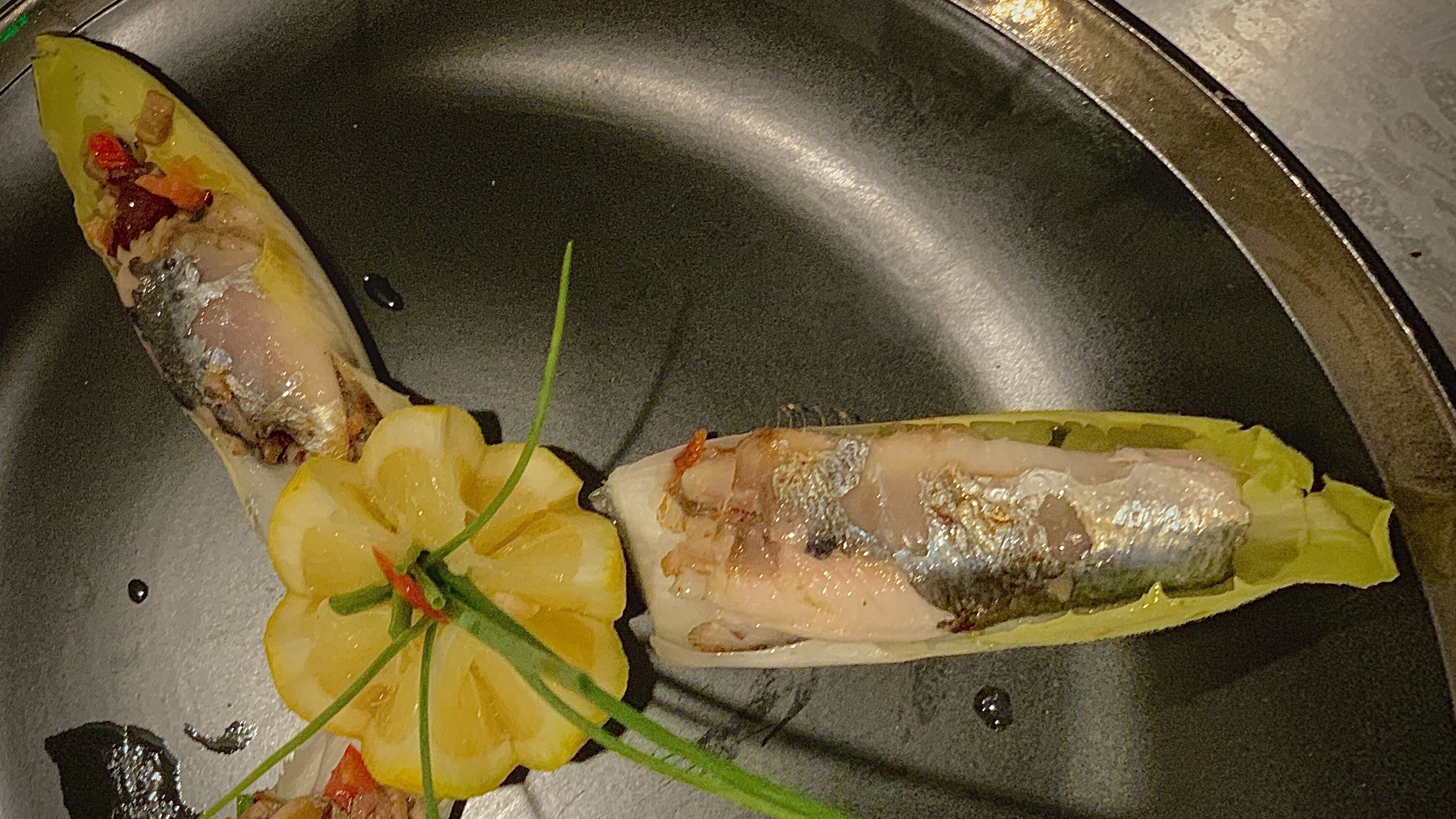 Dos filetes de pescado sobre un plato de metal con rodajas de limón y cebollines.
