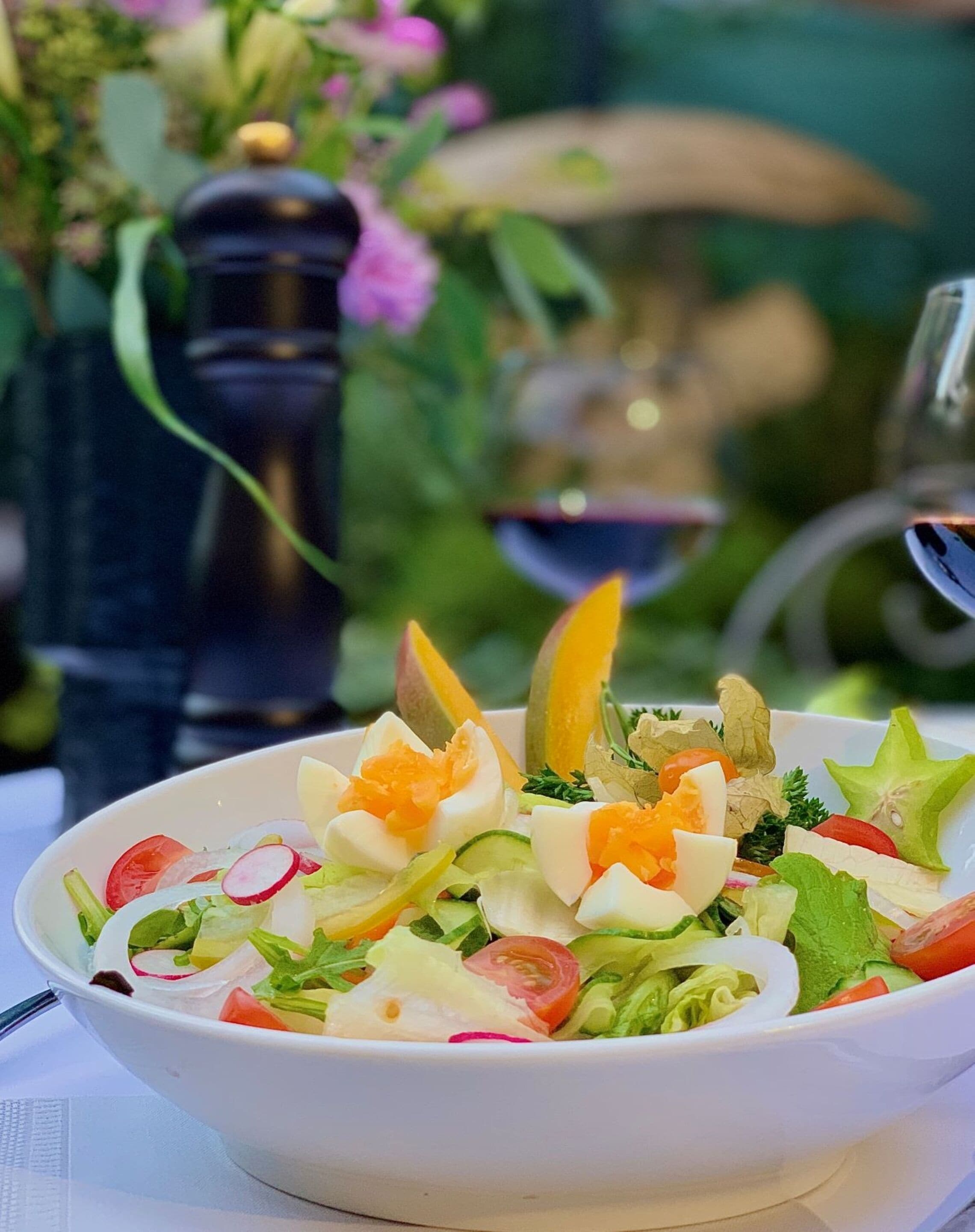 Insalata in una ciotola con diverse verdure e uova, su un tavolo con tovaglia bianca.
