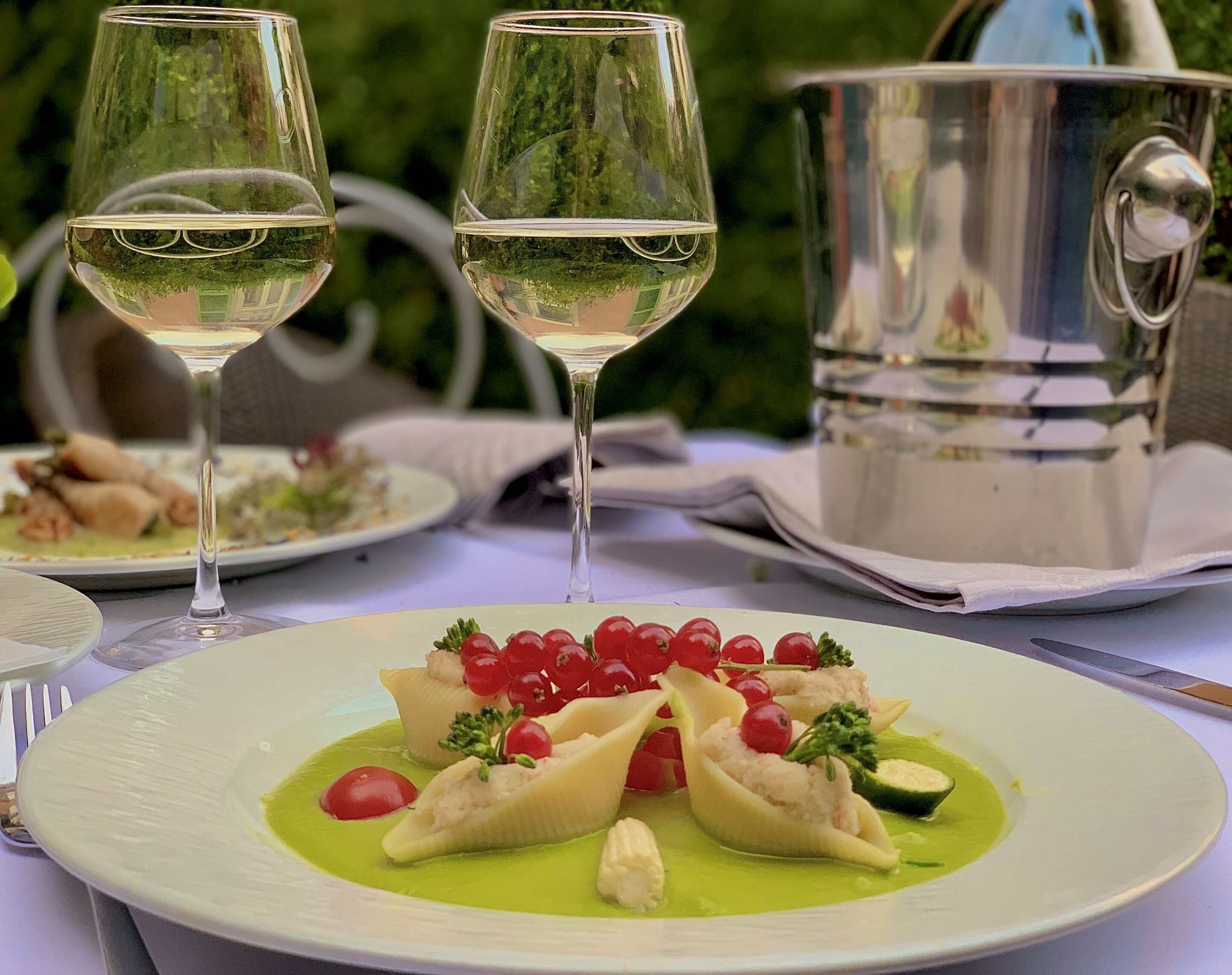 Une table à manger avec une assiette de raviolis, une bouteille de vin et un pot en argent.