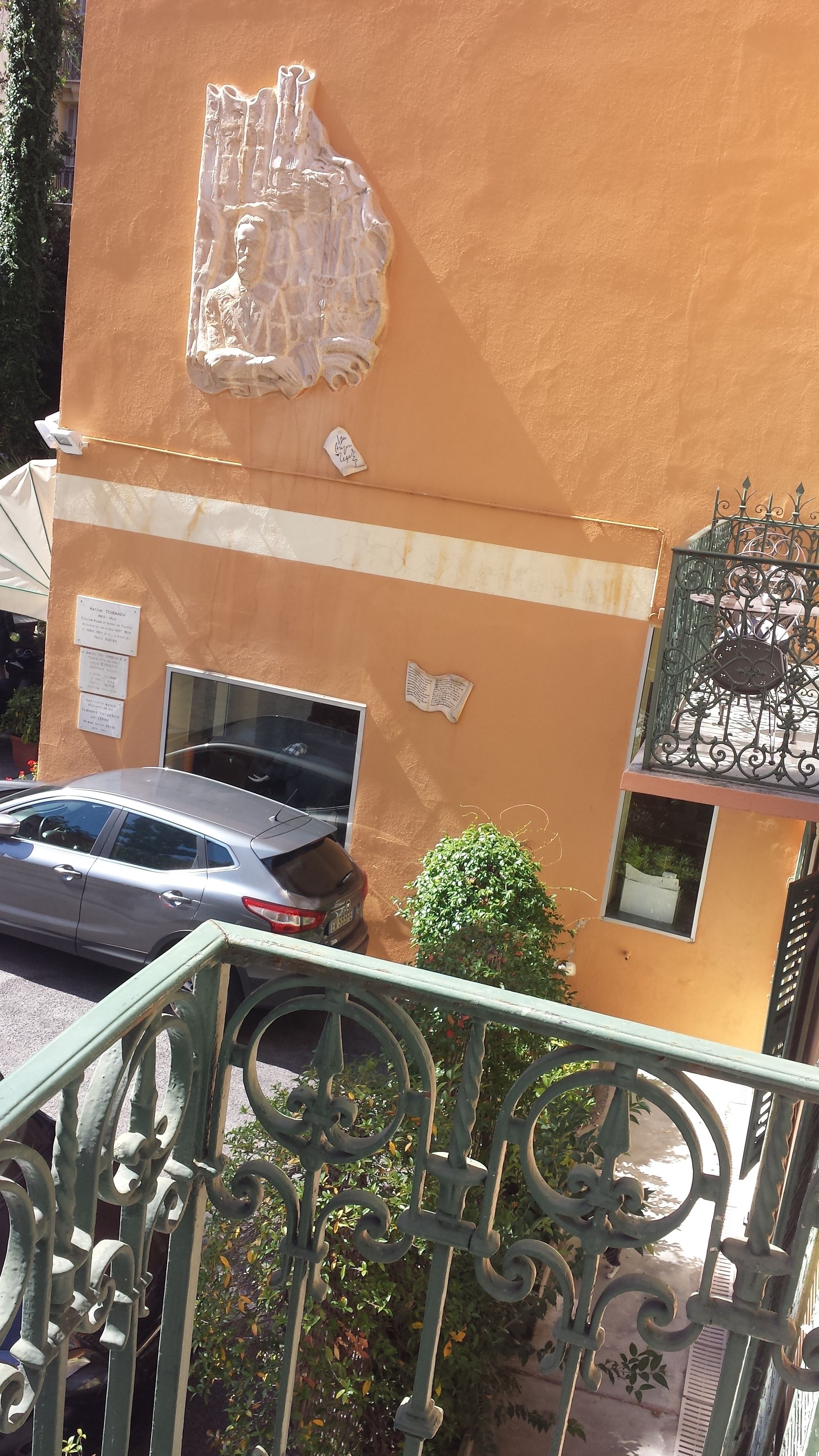 A building with a beige exterior, a balcony with ornate metal railings, and a parked car.