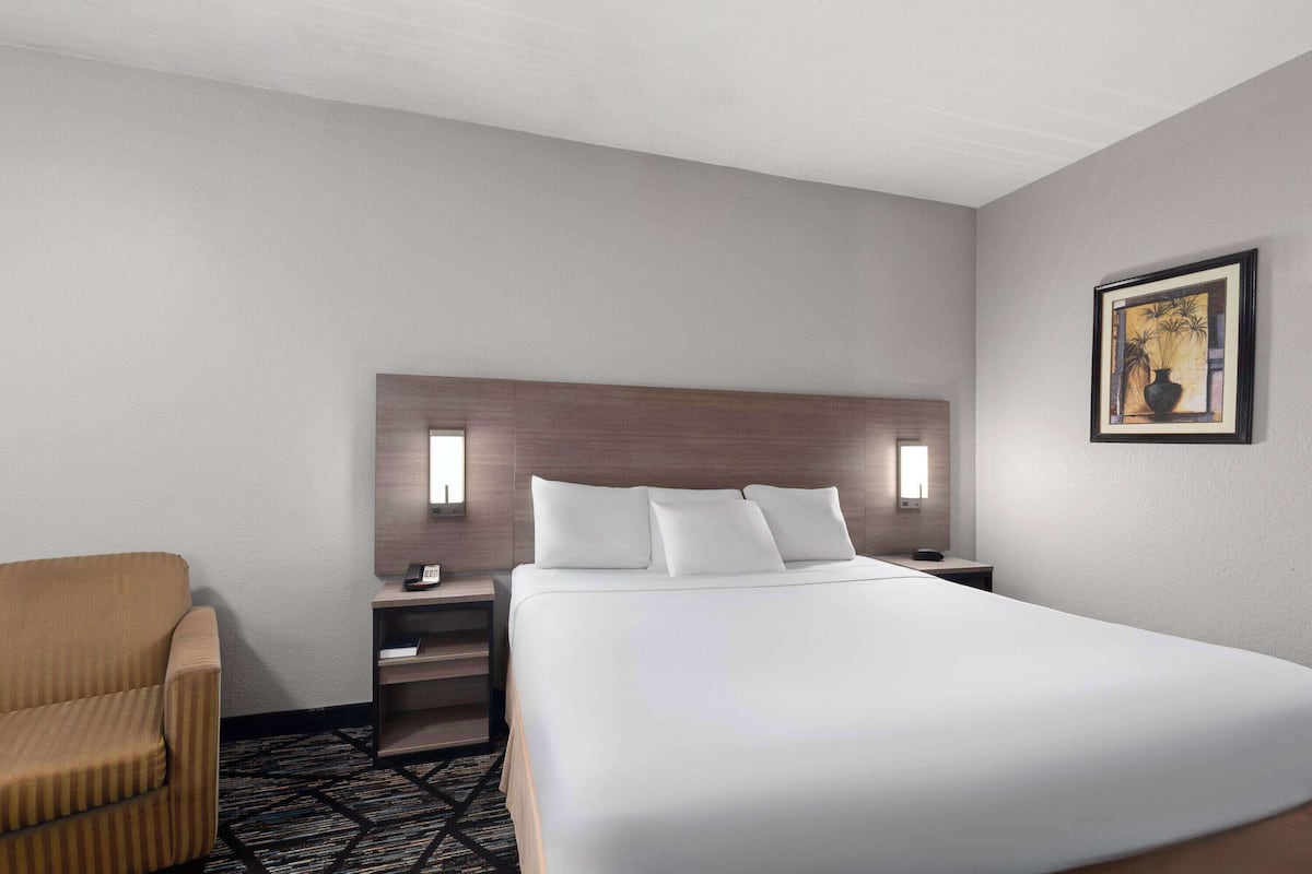 A hotel room with a large bed, a nightstand, a chair, and a painting on the wall.