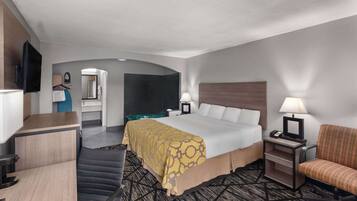 Une chambre d’hôtel comprenant un lit, un bureau, une chaise, une télévision et une salle de bain visible à travers une arche.