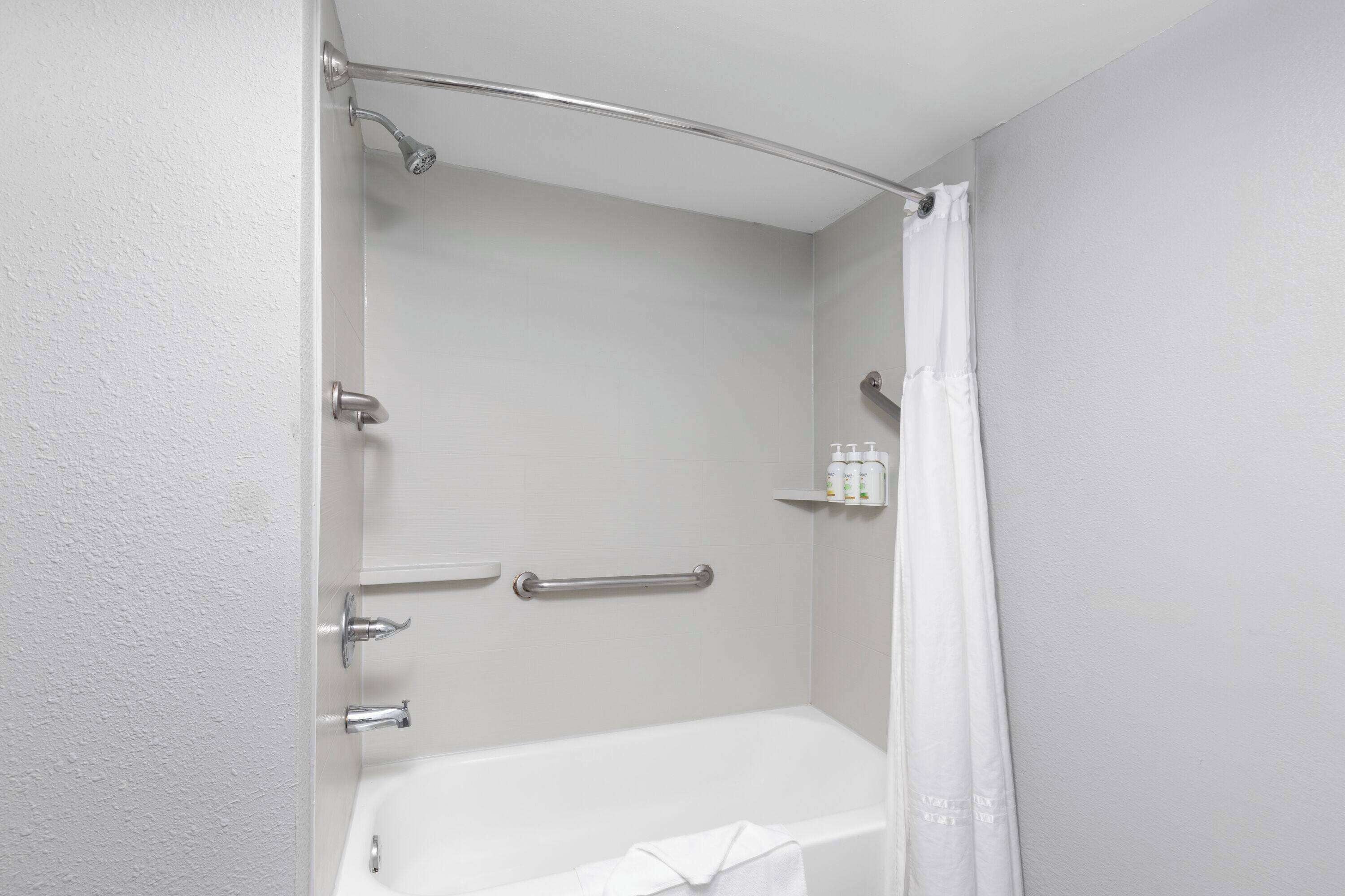 A bathroom with a bathtub, a shower, and a handrail.