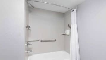 A bathroom with a bathtub, a shower, and a handrail.