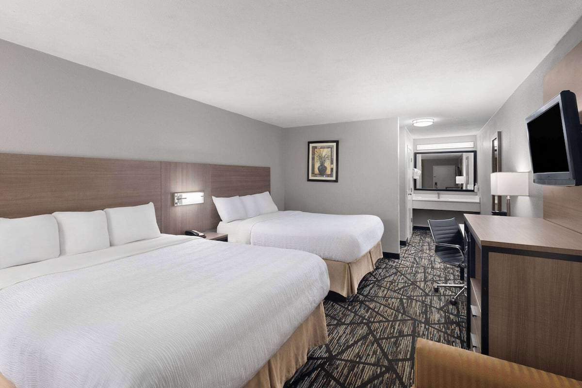 A hotel room with two beds, a desk, a chair, a television, and a bathroom visible through an open door.