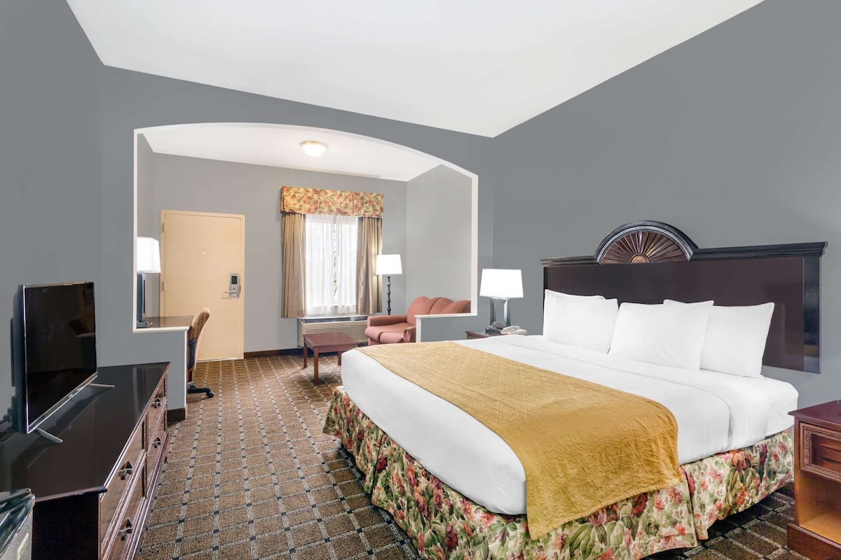 A hotel room with a bed, a desk, a TV, a chair, and a window with curtains.