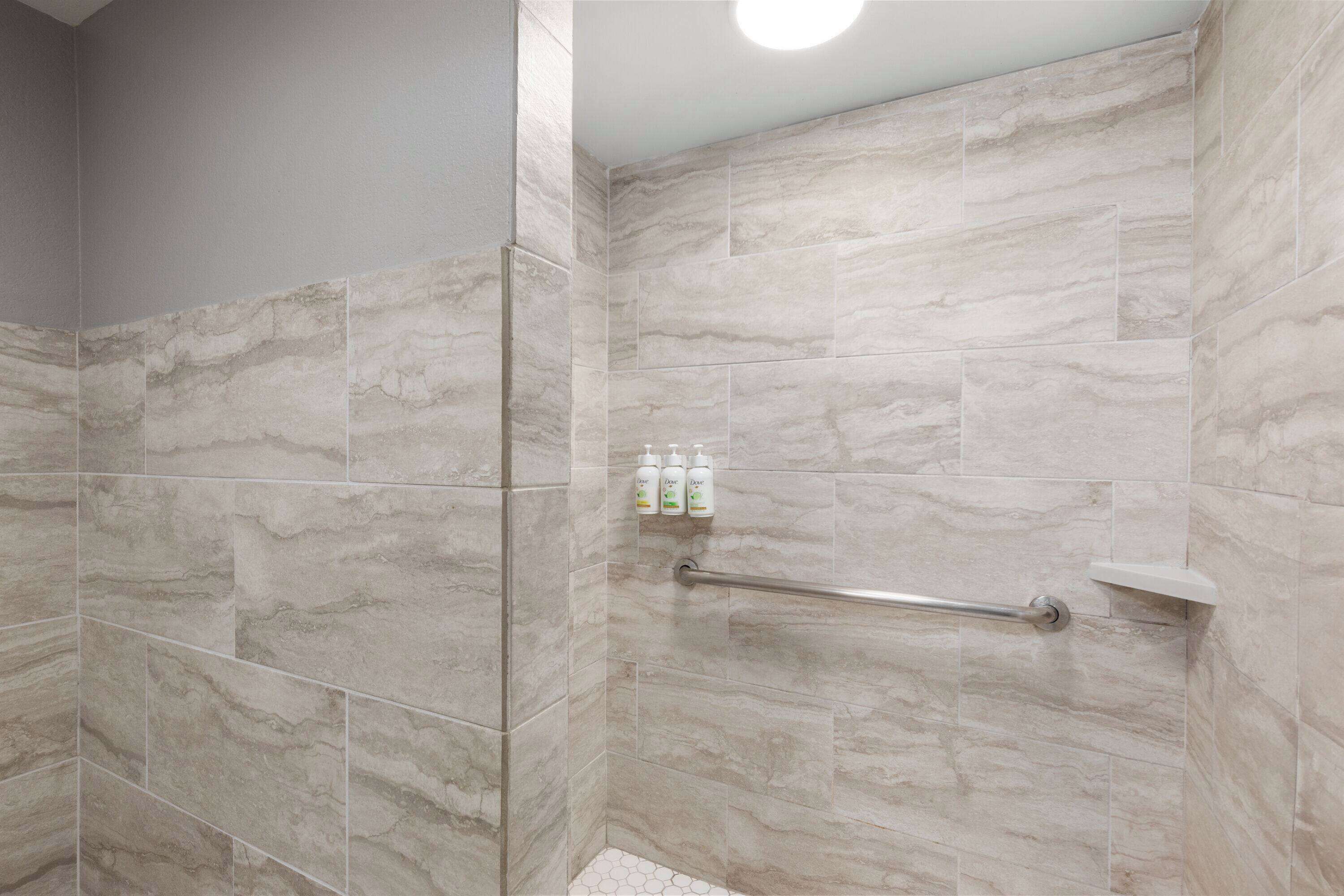 A shower area with marble tiles, a handrail, and toiletries on the wall.