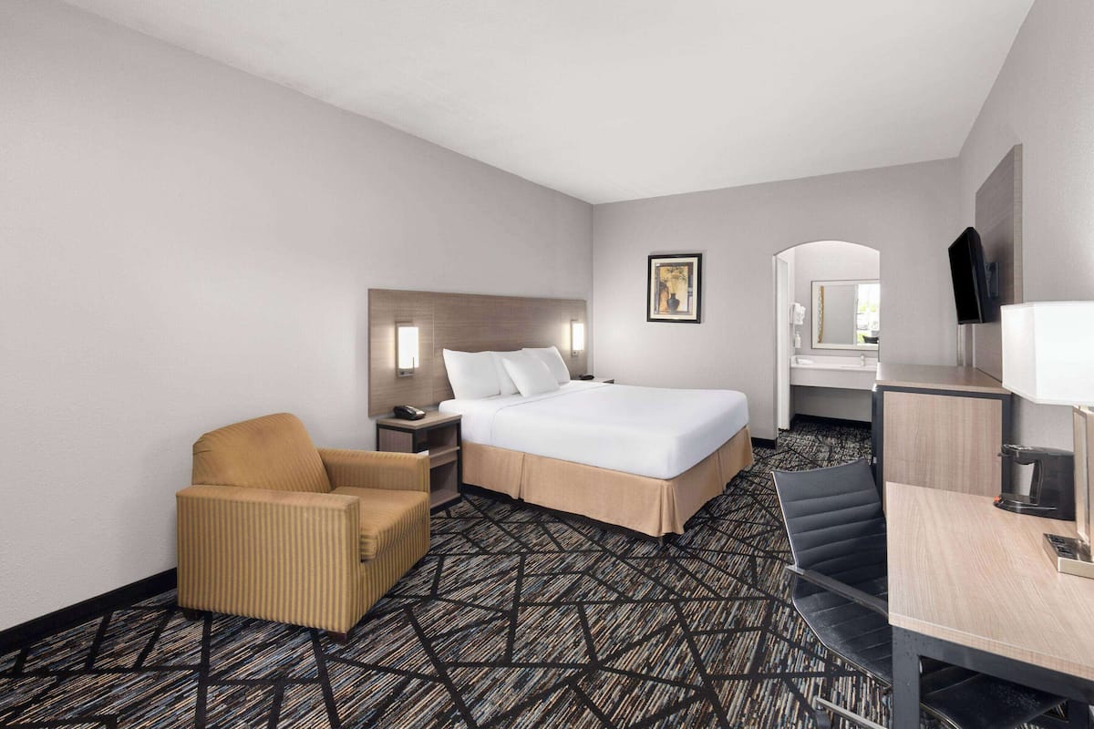 A hotel room with a bed, a chair, a desk, and a mirror.