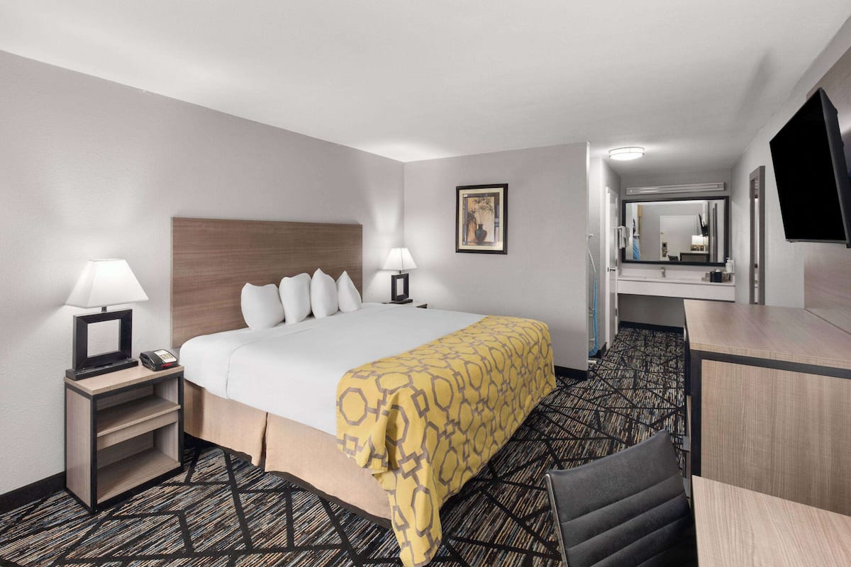 A hotel room with a bed, bedside tables with lamps, a desk, a chair, and a large mirror.