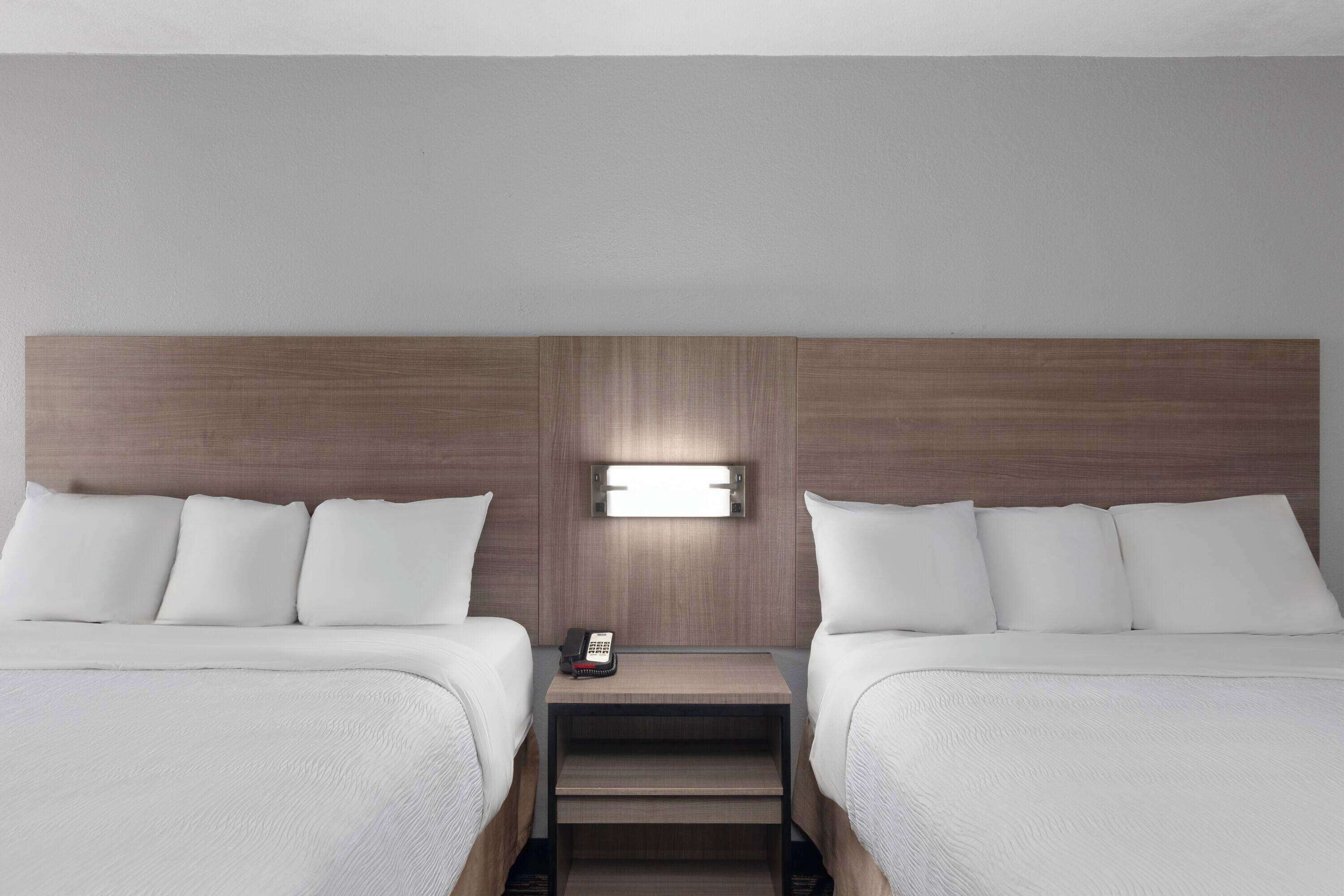 A hotel room with two beds, a nightstand with a phone, and a wall-mounted light.