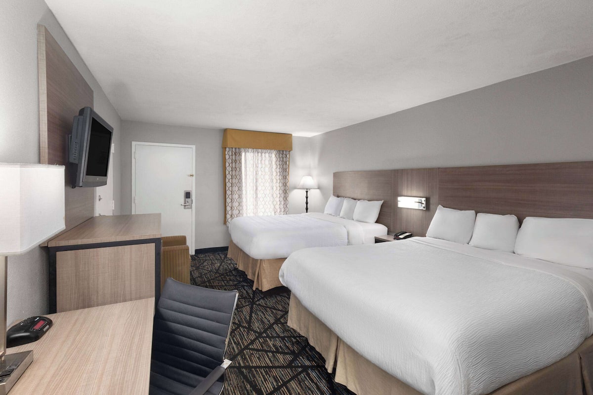 A hotel room with two beds, a desk, a TV, and a lamp.