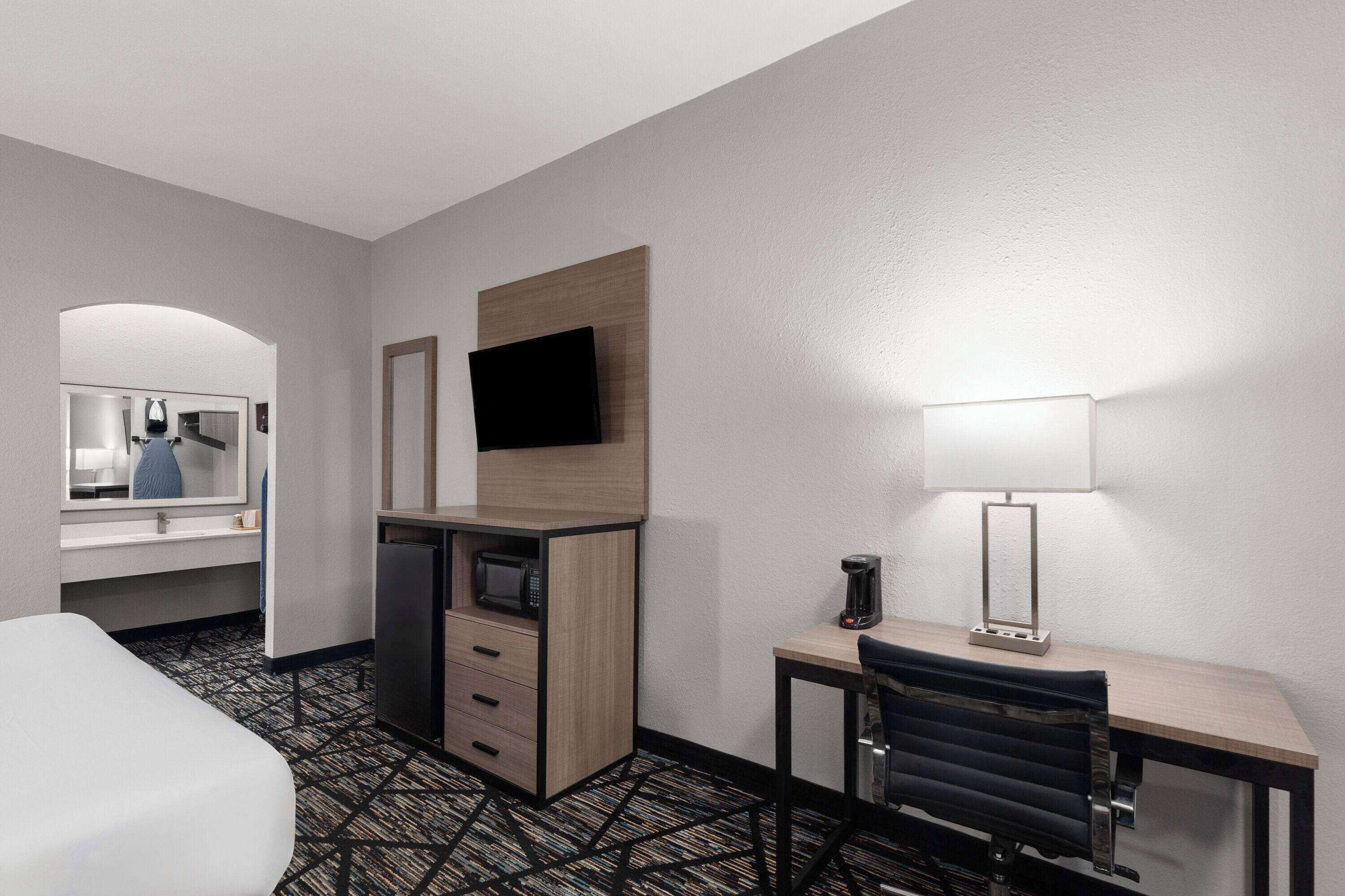 Une chambre d’hôtel équipée d’un lit, d’un bureau avec une chaise, d’un four à micro-ondes, d’une machine à café et d’un téléviseur à écran plat fixé au mur.