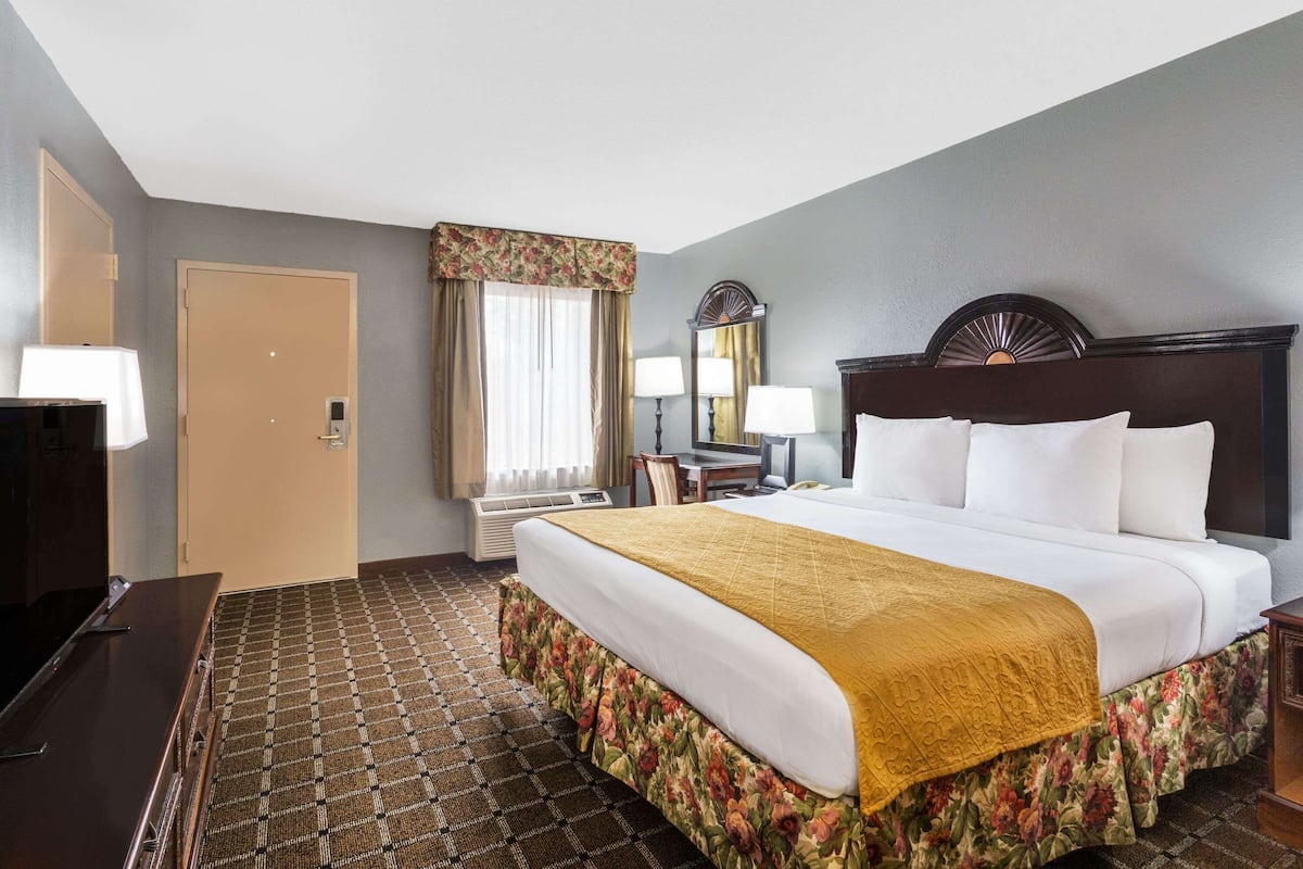 A hotel room with a bed, a desk, a chair, a TV, and a mirror.