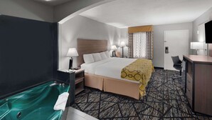 Une chambre d’hôtel comprenant un lit, des lampes de chevet, un bureau, une chaise, une salle de bain avec baignoire et une moquette à motifs.