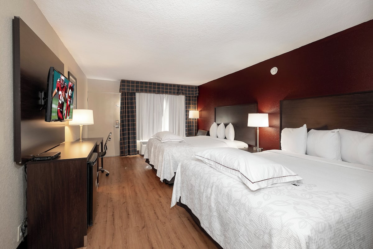 A hotel room with two beds, a desk, a TV, and a window with curtains.