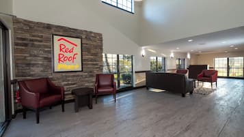 A spacious lobby with a stone wall, a Red Roof Plus sign, leather chairs, and a sofa.