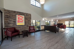 Un hall d’entrée spacieux avec un mur en pierre, une enseigne « Red Roof Plus », des fauteuils en cuir et un canapé.