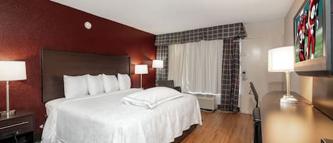 A hotel room with a large bed, two bedside lamps, a flat-screen TV, and a wooden floor.