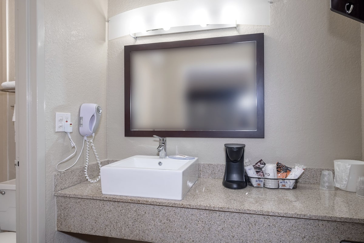 A bathroom with a white sink, a mirror, a hairdryer, a coffee maker, and toiletries on the counter.